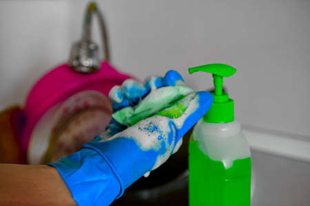 Close-up of hands in rubber gloves holding a sponge and squeezing out dishwashing liquid. Green detergent.の写真素材