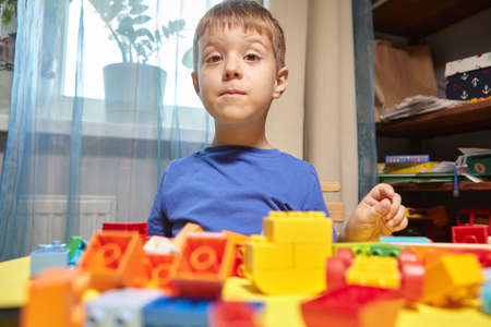 A beautiful boy is playing at home with building blocks. A cute smiling boy is playing with a constructor with a lot of colorful plastic blocks in the room, building a city. Preschool classes.の写真素材