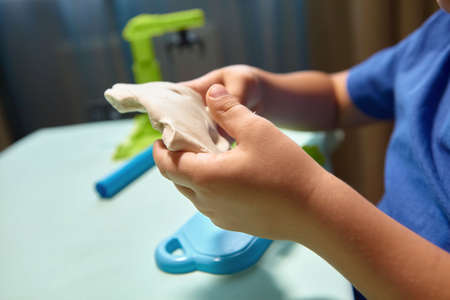 Child is sculpting with modeling clay. Art activity for children, indoor fun for kids concept. Close up and selective focus face and hands boy. Fun time for children activity at home or school.の写真素材