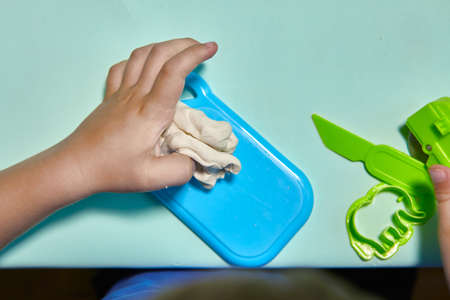 Child is sculpting with modeling clay. Art activity for children, indoor fun for kids concept. Close up and selective focus face and hands boy. Fun time for children activity at home or school.の写真素材