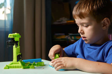 Child is sculpting with modeling clay. Art activity for children, indoor fun for kids concept. Close up and selective focus face and hands boy. Fun time for children activity at home or school.の写真素材