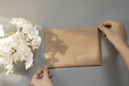 Hands holding an empty brown craft envelope of A5 format on a gray background. Top view of the layoutの写真素材