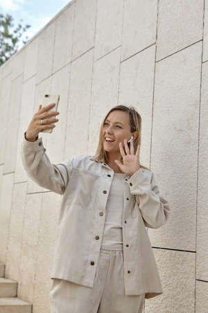 A young woman answers a video call. A woman with blonde hair wearing wireless headphones talking by video linkの写真素材