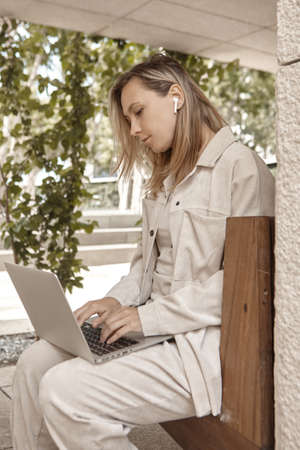 A young woman is working at a laptop in the park. The concept of remote work via the Internet. A freelancer works in the parkの写真素材