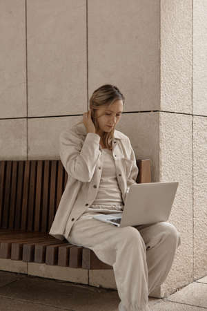 A young woman is working at a laptop in the park. The concept of remote work via the Internet. A freelancer works in the parkの写真素材