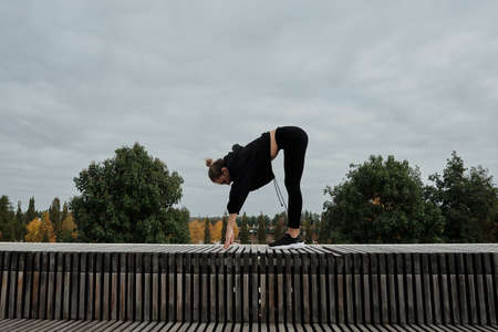 Middle-aged blonde caucasian woman athlete lady wears black tracksuit, on the site in city park runs...