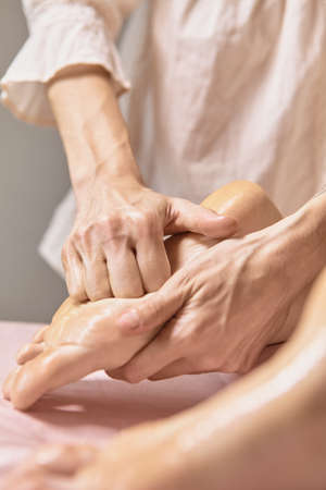 Close up reflexology foot massage. Professional therapist giving leg and foot massage to a woman in...