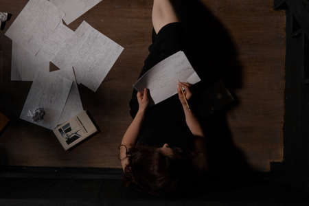 A woman in black clothes is sitting on the floor, sheets are scattered next to her. The process of writing a text, a creative crisis.の写真素材