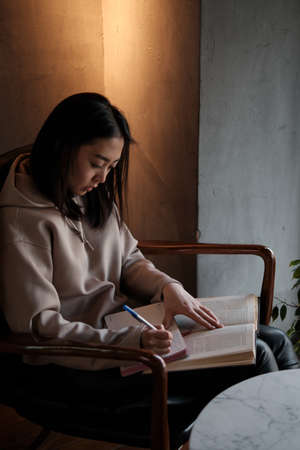 Shot of young asian female student sitting at table and writing on notebook. Young female student studying in cafe.の写真素材