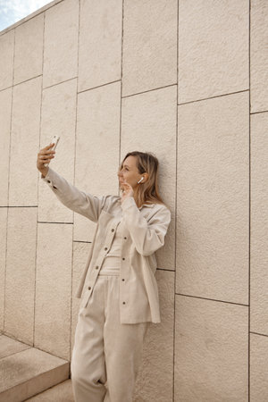 A young woman answers a video call. A woman with blonde hair wearing wireless headphones talking by video linkの写真素材