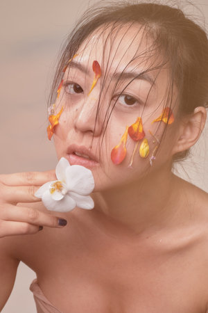 Attractive young Asian woman with flowers. Stunning brunette girl with flowers on the face. Close up face of young beautiful woman with a healthy clean skin. Pretty woman with floral makeup.の写真素材