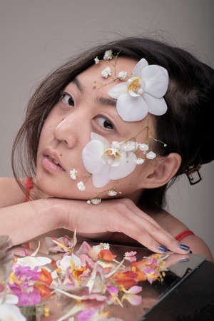 Attractive young Asian woman with flowers. Stunning brunette girl with flowers on the face. Close up face of young beautiful woman with a healthy clean skin. Pretty woman with floral makeup.の写真素材