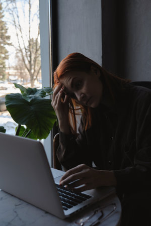 a red-haired freelance woman with glasses works remotely on a laptop in a cafe.xの写真素材