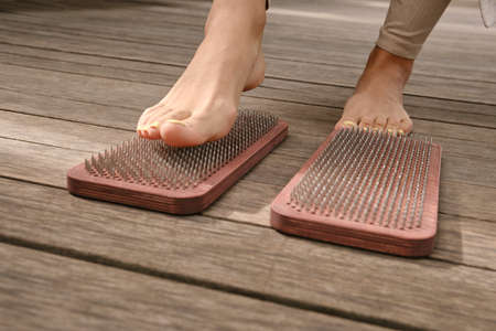 The practice of self-knowledge in the park. A woman with a pedicure stands on sharp nails. Female legs and Sadhu board close-up. Yoga. Meditation.の写真素材