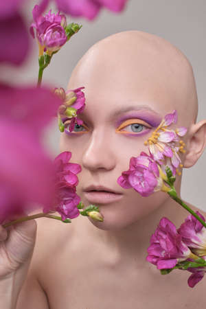 A beautiful woman without hair with flowers on her head, a conceptual photo with an unusual modelの写真素材