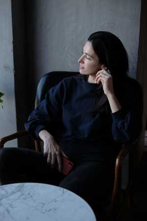 A brunette woman is sitting at a table in a cafe with a phone in her hands and looking at the cameraの写真素材