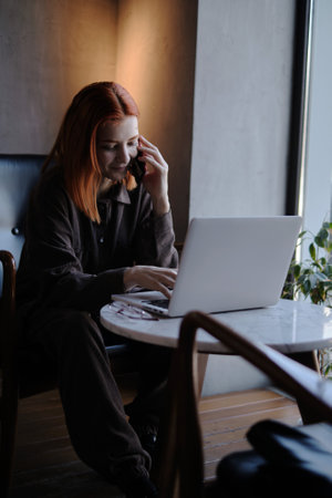 a red-haired freelance woman with glasses works remotely on a laptop in a cafe.xの写真素材