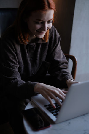 a red-haired freelance woman with glasses works remotely on a laptop in a cafe.xの写真素材