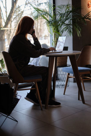a red-haired freelance woman with glasses works remotely on a laptop in a cafe.の写真素材