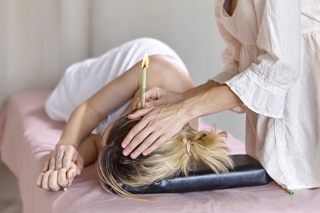 Beautiful woman ear receiving candle treatment. Therapist performing an ear wax treatment on a patient using candling. Naked woman receiving ear candle treatment from masseurの写真素材