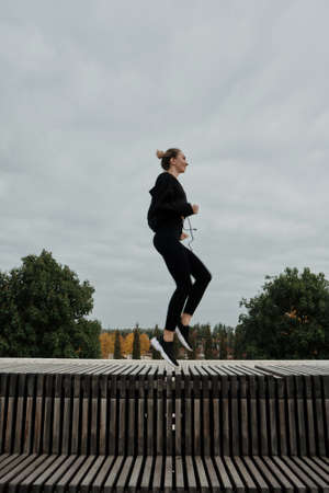 Middle-aged blonde caucasian woman athlete lady wears black tracksuit, in city park run. Workout sport outdoors.の写真素材