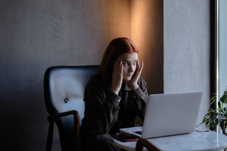 a red-haired freelance woman with glasses works remotely on a laptop in a cafe.xの写真素材