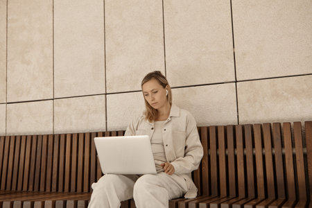 A young woman is working at a laptop in the park. The concept of remote work via the Internet. A freelancer works in the parkの写真素材