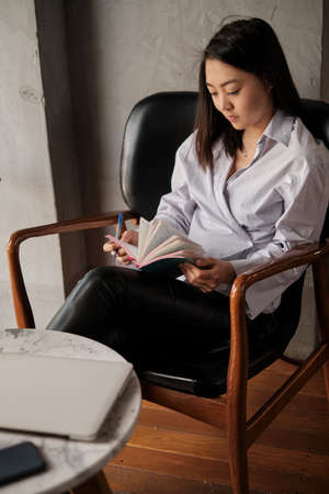 Asian female sitting in cafe, holding phone and pencil writing notebook
