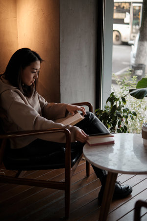 Shot of young asian female student sitting at table and writing on notebook. Young female student studying in cafe.の写真素材