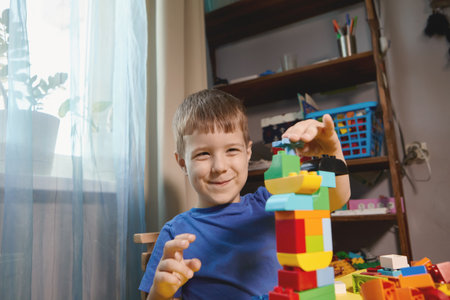 A beautiful boy is playing at home with building blocks. A cute smiling boy is playing with a constructor with a lot of colorful plastic blocks in the room, building a city. Preschool classes.の写真素材