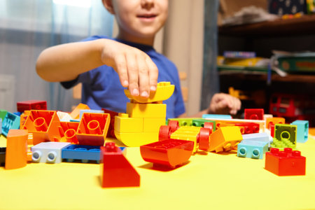 A beautiful boy is playing at home with building blocks. A cute smiling boy is playing with a constructor with a lot of colorful plastic blocks in the room, building a city. Preschool classes.の写真素材