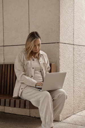 A young woman is working at a laptop in the park. The concept of remote work via the Internet. A freelancer works in the parkの写真素材