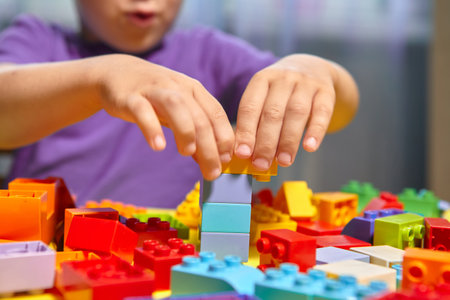 A beautiful boy is playing at home with building blocks. A cute smiling boy is playing with a constructor with a lot of colorful plastic blocks in the room, building a city. Preschool classes.の写真素材