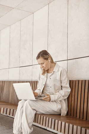 A young woman is working at a laptop in the park. The concept of remote work via the Internet. A freelancer works in the parkの写真素材