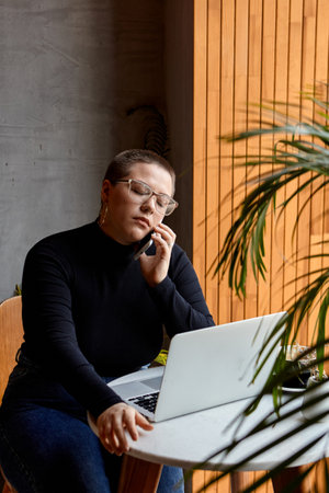 Young girl with short hair and nose piercing sits in a cafe. A woman is talking on the phone and work at a tablet. The concept of freelancing and remote work.の写真素材