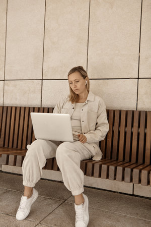 A young woman is working at a laptop in the park. The concept of remote work via the Internet. A freelancer works in the parkの写真素材