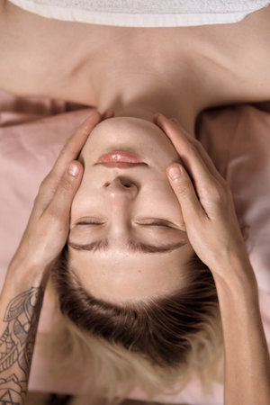 Young beautiful woman is getting a relaxing head and face massage in wellness center. Masseur doing massage the head of an young beautiful girl woman in the spa salon close up macroの写真素材