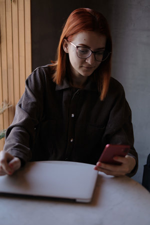 a red-haired freelance woman with glasses works remotely on a laptop in a cafe.xの写真素材