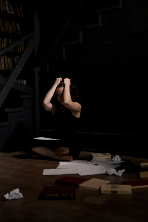 A woman in black clothes is sitting on the floor, sheets are scattered next to her. The process of writing a text, a creative crisis.の写真素材