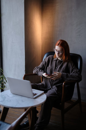 a red-haired freelance woman with glasses works remotely on a laptop in a cafe.xの写真素材