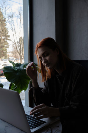 a red-haired freelance woman with glasses works remotely on a laptop in a cafe.xの写真素材