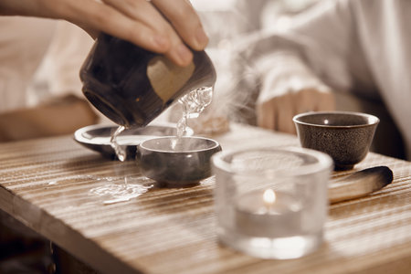 A close-up shot of a Chinese tea ceremony. On the table there is a gaiwan, bowls, a tea keeper and a palo santoの写真素材