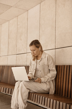 A young woman is working at a laptop in the park. The concept of remote work via the Internet. A freelancer works in the parkの写真素材