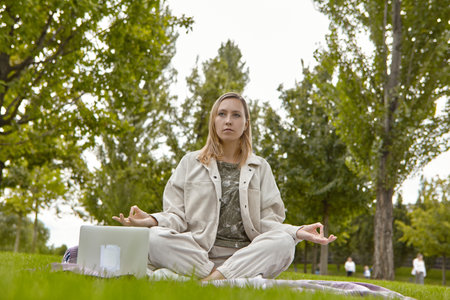Woman sitting in lotus pose, crossed leg posture (Sukhasana) and meditating in a park. An attractive woman relieves stress by meditating in the parkの写真素材