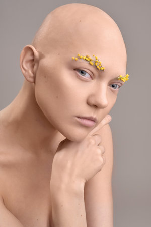 A beautiful woman without hair with flowers on her head, a conceptual photo with an unusual modelの写真素材
