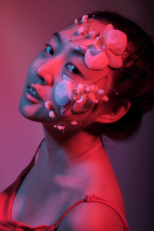 Attractive young Asian woman with flowers. Stunning brunette girl with flowers on the face. Close up face of young beautiful woman with a healthy clean skin. Pretty woman with floral makeup.の写真素材
