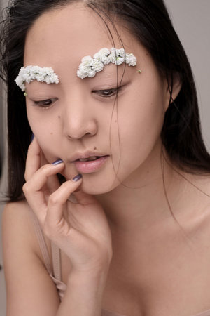 Attractive young Asian woman with flowers. Stunning brunette girl with flowers on the face. Close up face of young beautiful woman with a healthy clean skin. Pretty woman with floral makeup.の写真素材