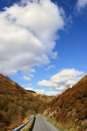 Narrow mountain road with hills on either side and a blue sky with puffy white clouds in the distance. Set in the Cambrian Mountains, Wales, UK.の写真素材