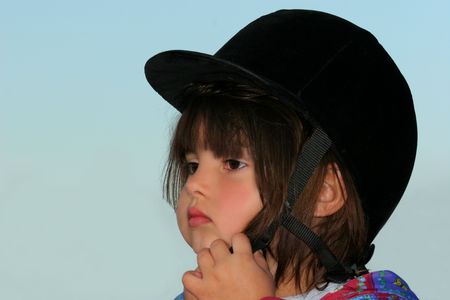 Little girl putting on a black velvet riding hat against a  pale blue sky.の写真素材