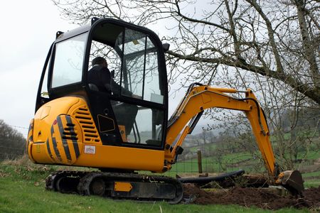 Man in a mini digger digging a trench in a field.